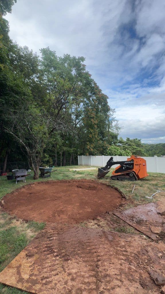 Excavation site with a skid steer loader preparing ground for landscaping changes.