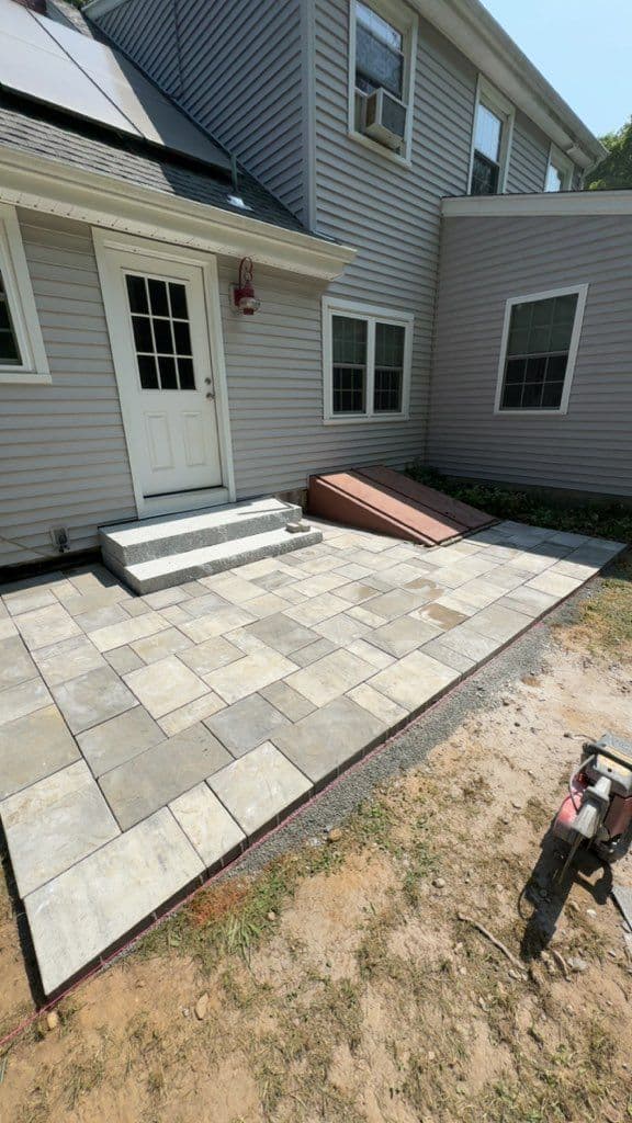Paved patio area with steps and ramp beside a residential grey house.