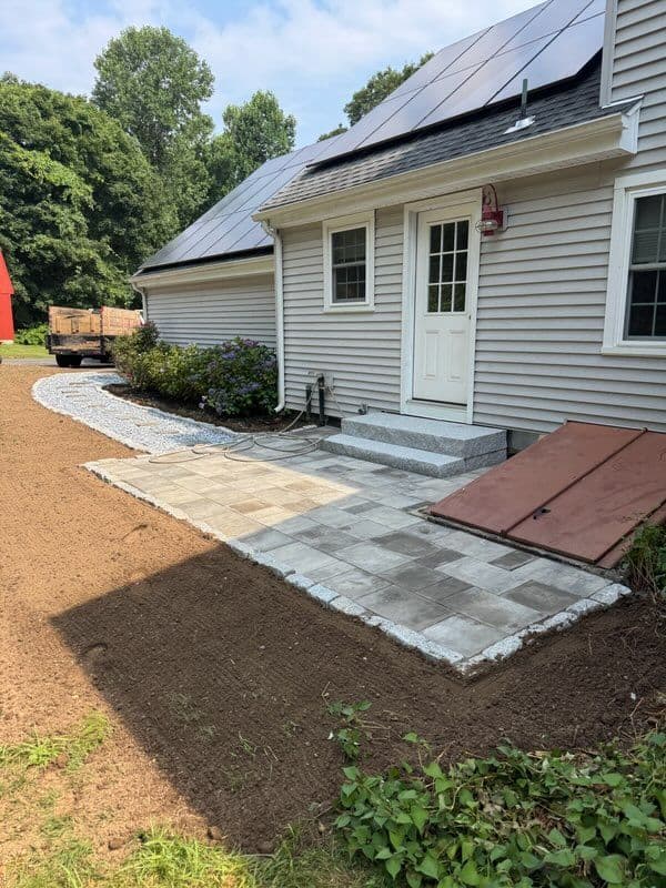 Newly laid patio with pavers beside a house, surrounded by landscaping and gravel.