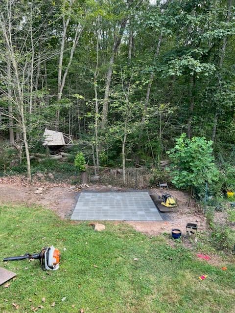 cleared outdoor area with a concrete slab surrounded by trees and landscaping equipment