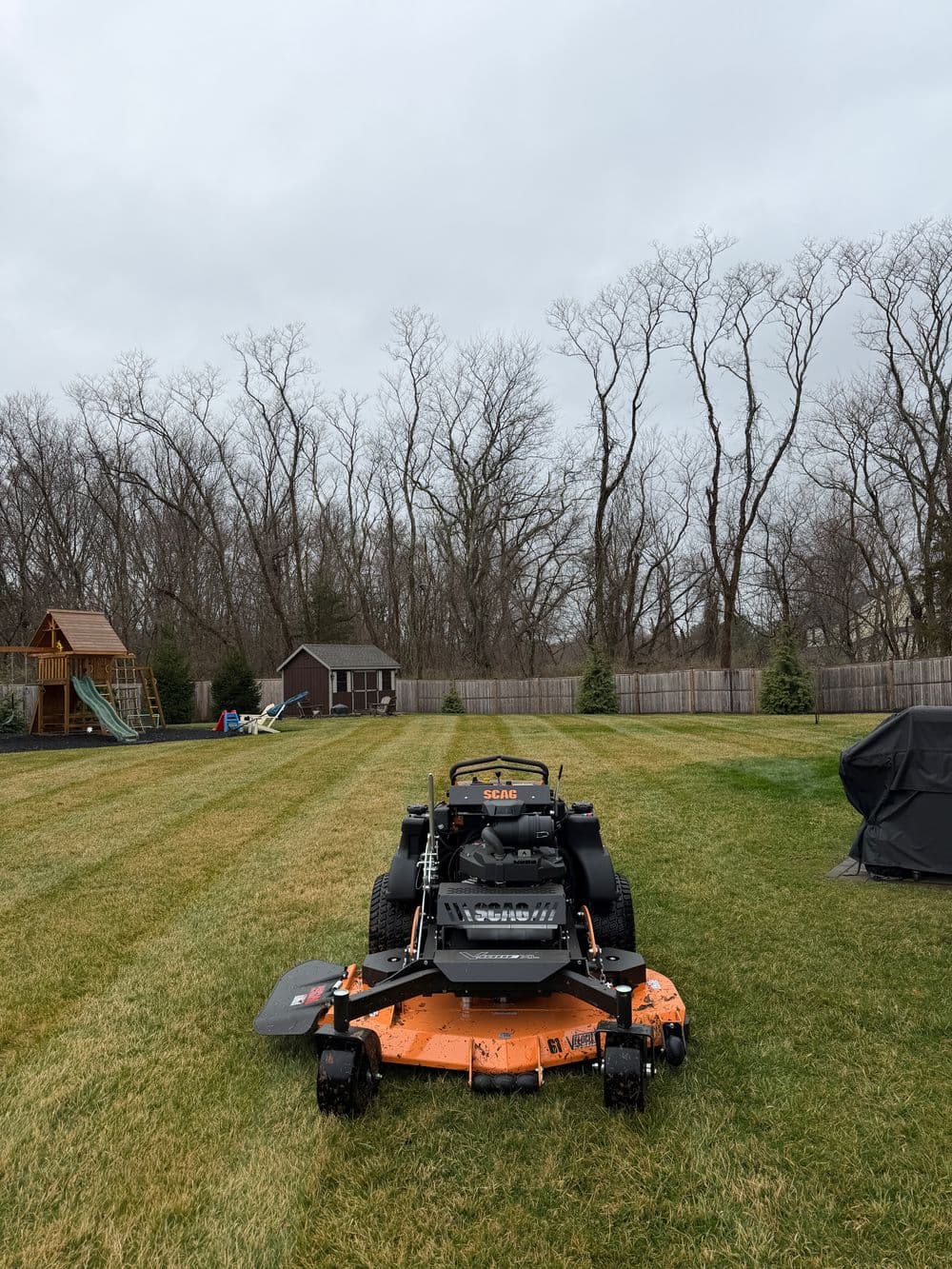 Zero-turn lawn mower on freshly mowed grass with a playground in the background.
