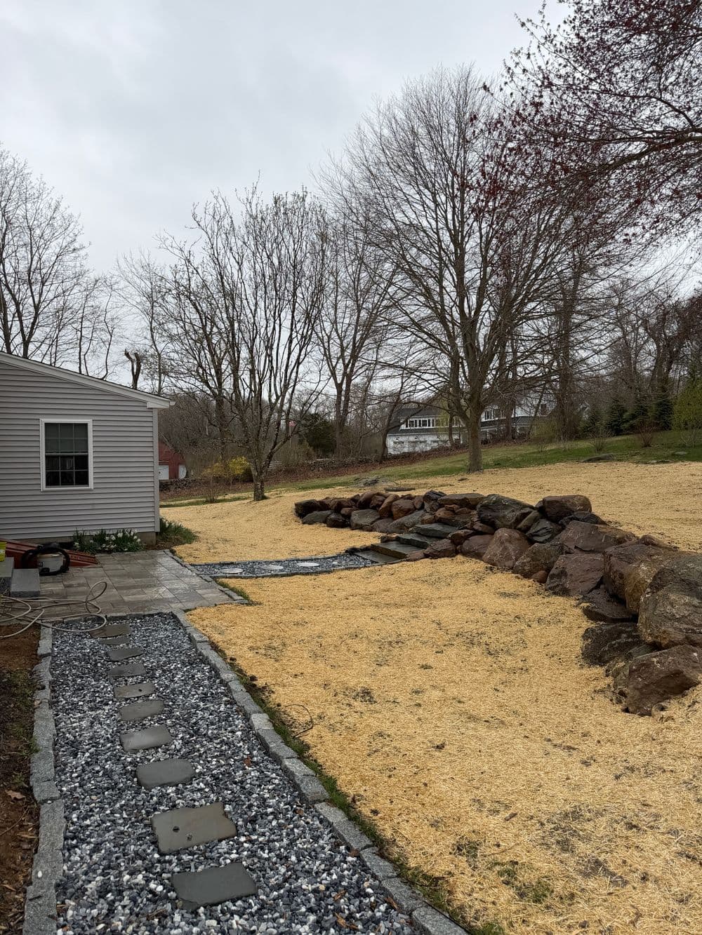 Pathway leading to a landscaped yard with boulders and recently laid straw on grass.