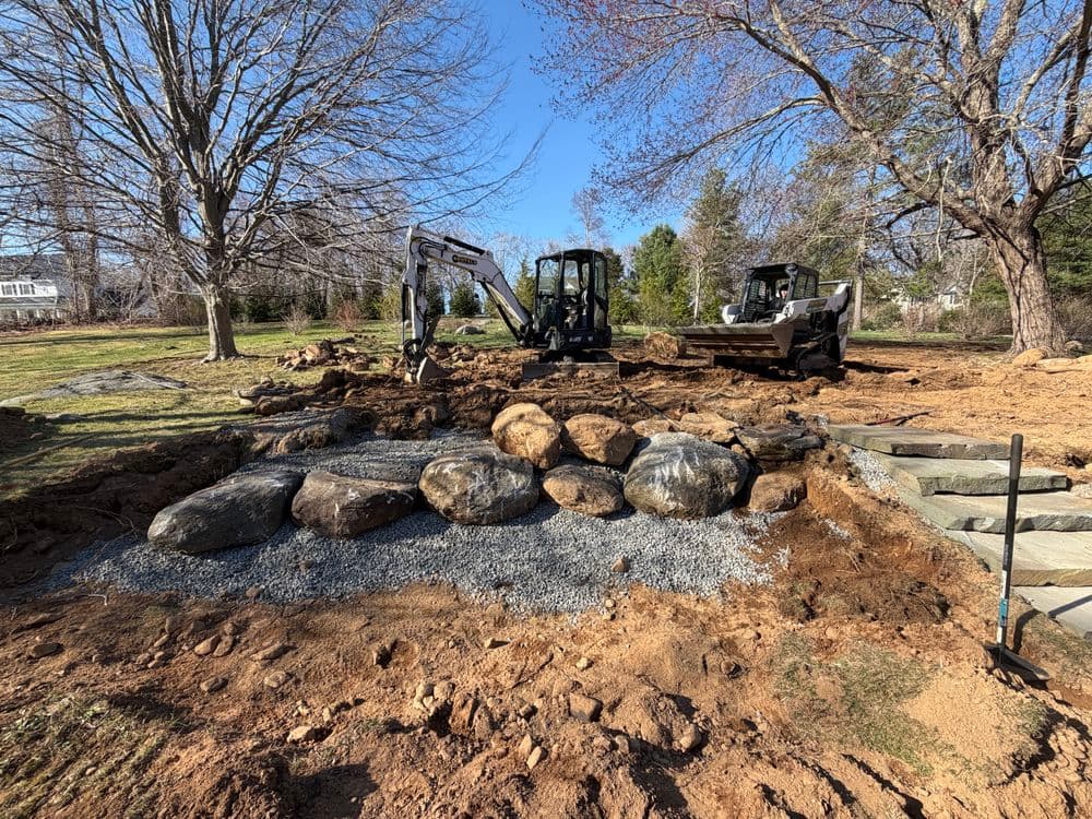 Excavation equipment and rocks in a residential landscape under construction.