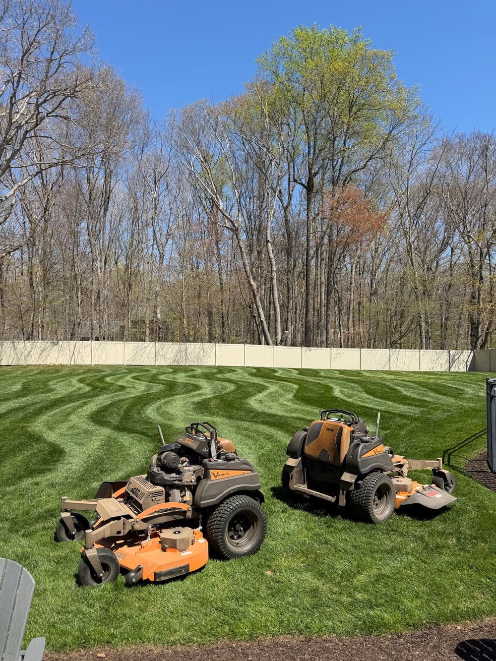 Lawn care scene with two riding mowers on freshly striped grass under a clear blue sky.