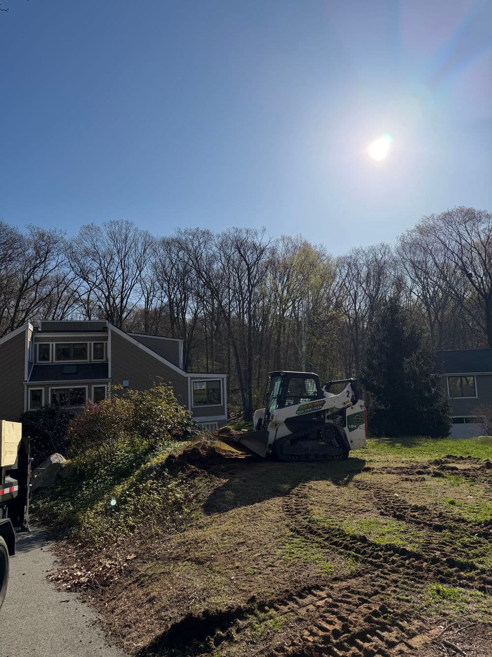 Excavator on a residential property with trees and clear blue sky in the background.