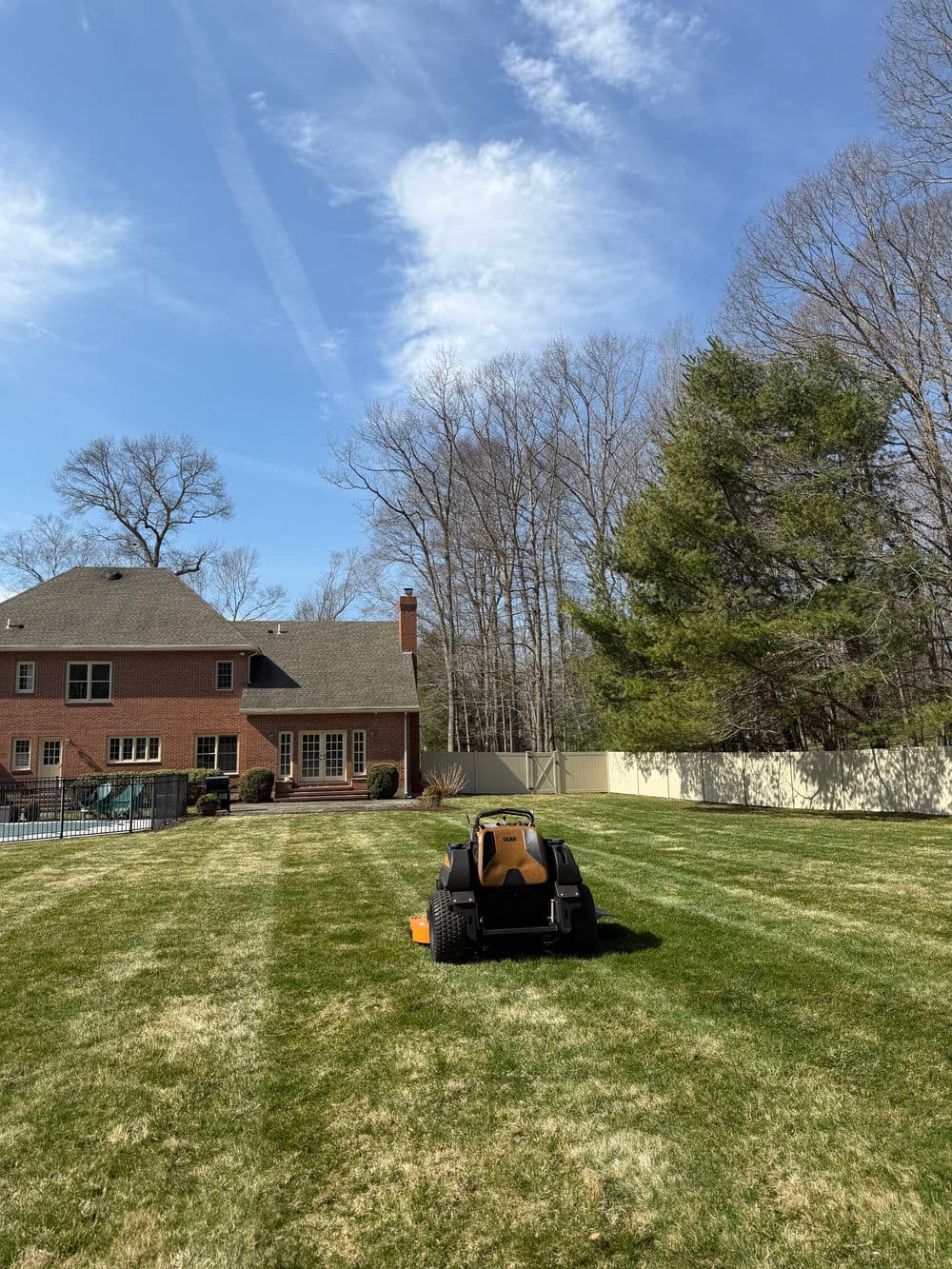 Lawn care robot mowing a green yard beside a brick house on a sunny day.