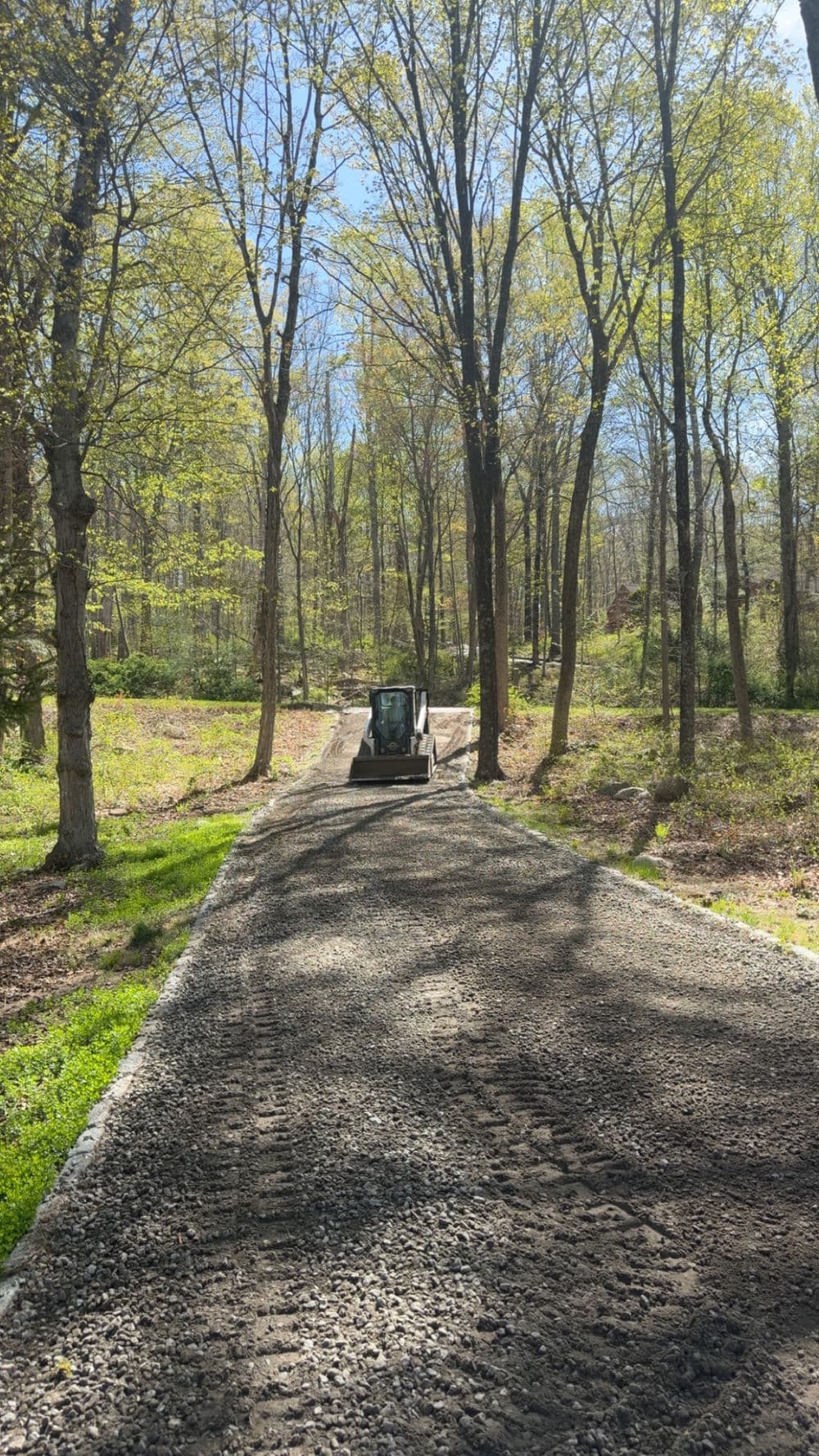 Small construction vehicle on gravel path surrounded by green trees in a sunny forest.
